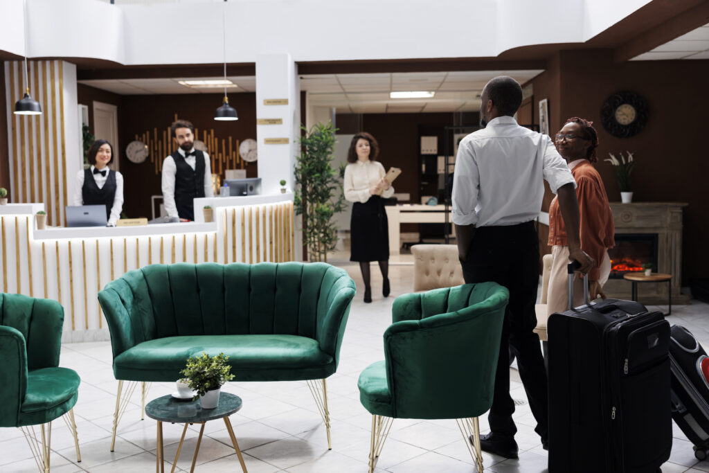 African american couple at reception, arriving at hotel and preparing to do check in process. Happy man and woman asking front desk staff about room reservation, fill in registration forms.