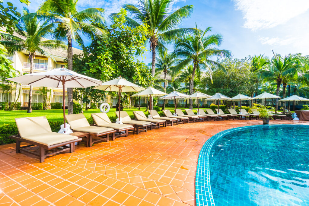 Beautiful luxury umbrella and chair around outdoor swimming pool in hotel and resort with coconut palm tree on blue sky - Boost up color Processing